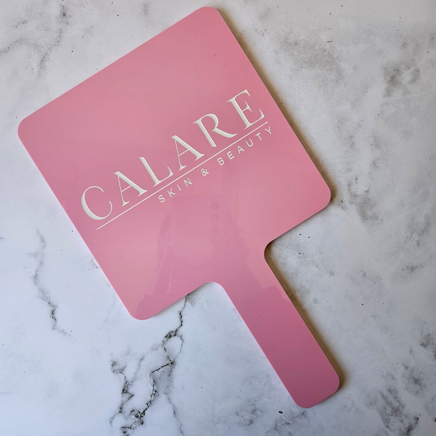 Square handheld mirror in pink gloss acrylic with white logo engraving for skin and beauty salon australia