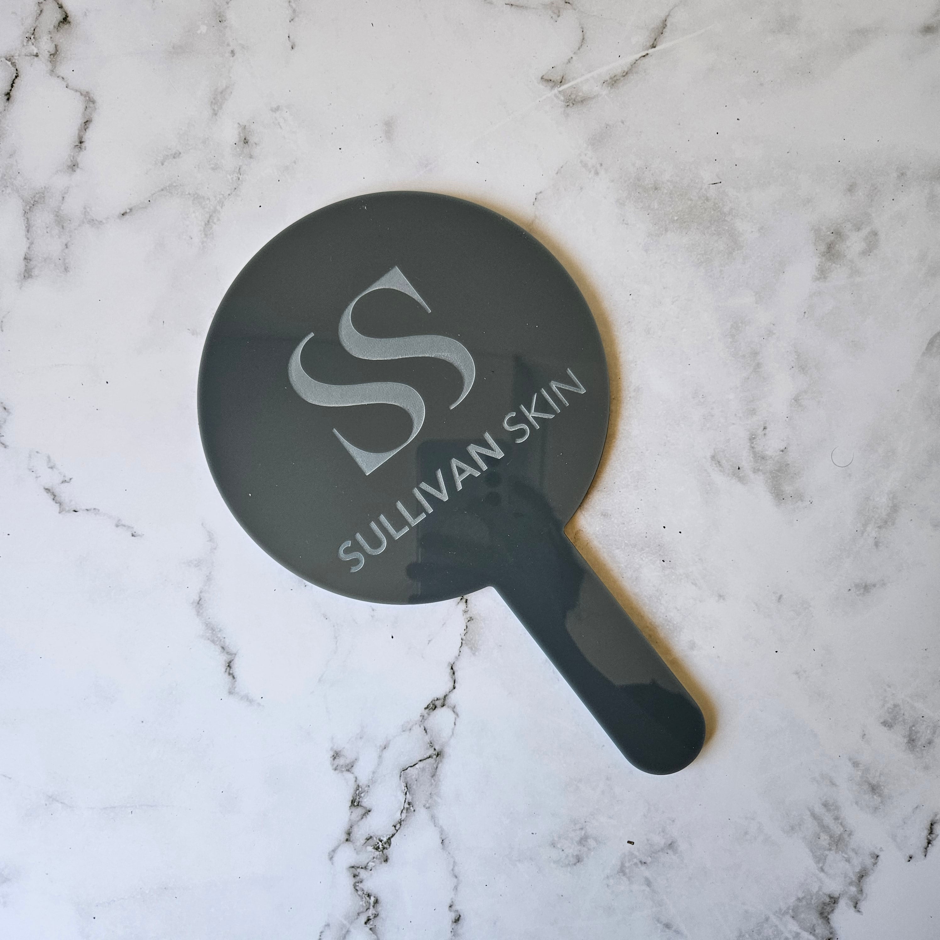 Round handheld mirror in grey gloss acrylic with custom logo engraving for skin and injectable clinic australia