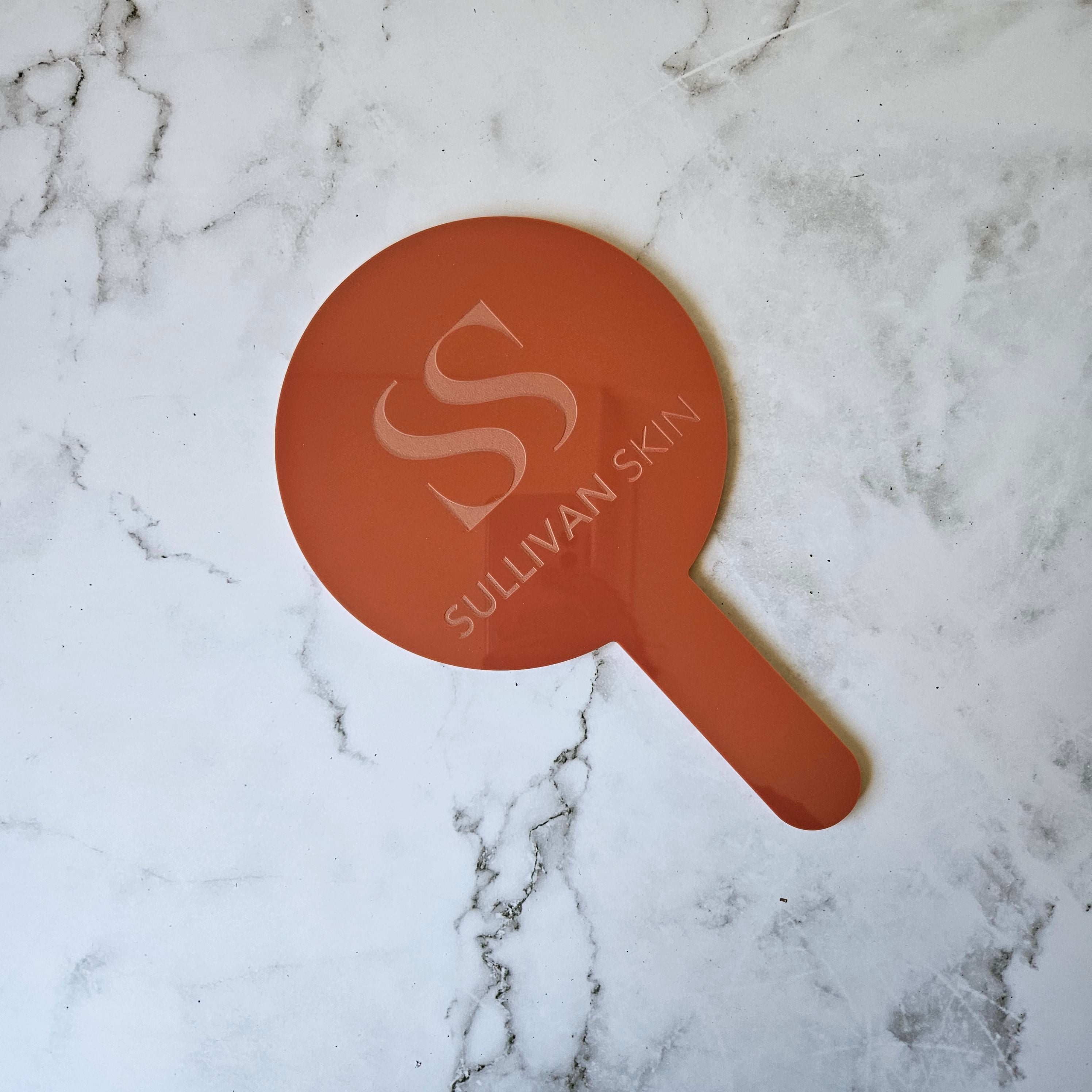 Round handheld mirror in terracotta red with custom logo engraving for skin clinic and injectable nurse