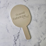 Oval handheld mirror in nude acrylic and metallic gold logo