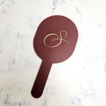 Oval handheld mirror with a personalised gold logo and cherry acrylic